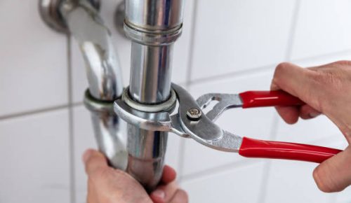Close-up Of A Plumber’s Hand Repairing Sink With Adjustable Wrench Close-up Of A Plumber's Hand Repairing Sink With Adjustable Wrench